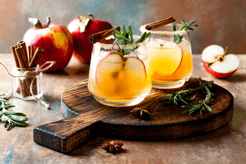 fall cocktails on a wooden board surrounded by apples and cinnamon sticks
